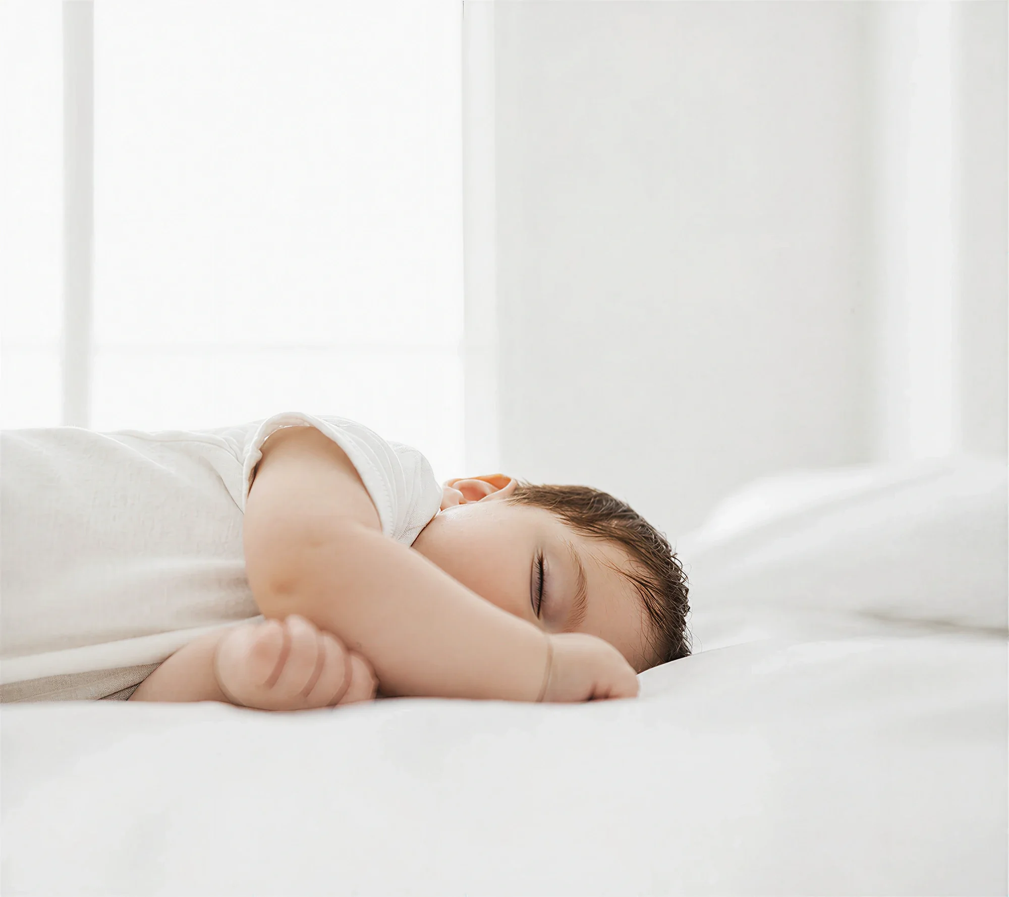 Sleeping baby resting peacefully on a white bed in soft natural light